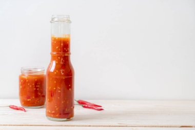 Şişede kırmızı biber ya da kırmızı biber sosu ve arka planda kavanoz.