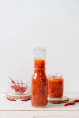 Şişede kırmızı biber ya da kırmızı biber sosu ve arka planda kavanoz.