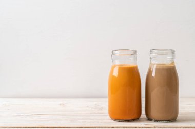 Tahta masanın üstünde süt şişeli Thai sütlü çay ve kahve.