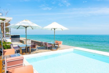 Yüzme havuzu ve tatil konsepti için deniz sahili geçmişi olan güzel, boş sandalye ve şemsiye.