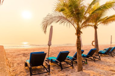 Güneş doğarken palmiye ağacı ve deniz plajı olan şemsiye koltuğu plajı - tatil ve tatil konsepti