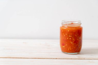 Şişede kırmızı biber ya da kırmızı biber sosu ve arka planda kavanoz.