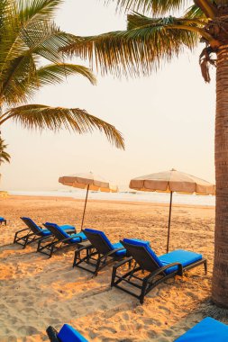 Güneş doğarken palmiye ağacı ve deniz plajı olan şemsiye koltuğu plajı - tatil ve tatil konsepti