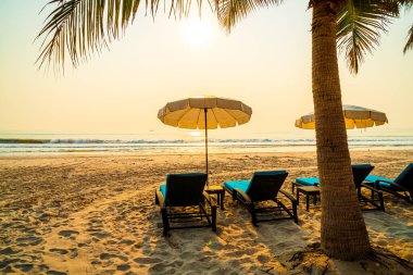 Güneş doğarken palmiye ağacı ve deniz plajı olan şemsiye koltuğu plajı - tatil ve tatil konsepti