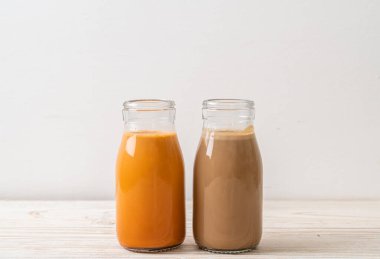 Tahta masanın üstünde süt şişeli Thai sütlü çay ve kahve.