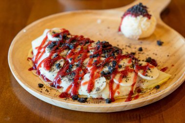 Muzlu krep, krema ve ahşap tabakta çilek sosu.