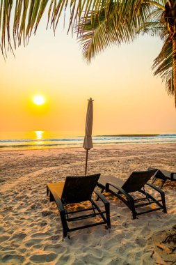 Güneş doğarken palmiye ağacı ve deniz plajı olan şemsiye koltuğu plajı - tatil ve tatil konsepti