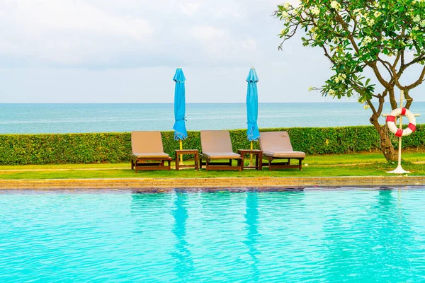 Sandalye havuzu ve şemsiyeyle okyanus arka planında yüzme havuzu