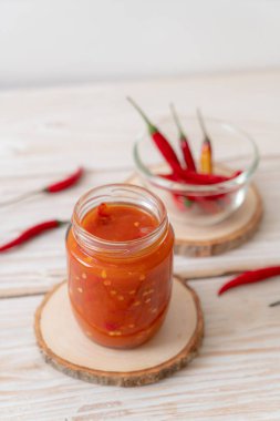 Şişede kırmızı biber ya da kırmızı biber sosu ve arka planda kavanoz.