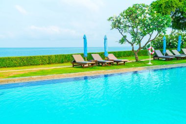 Sandalye havuzu ve şemsiyeyle okyanus arka planında yüzme havuzu