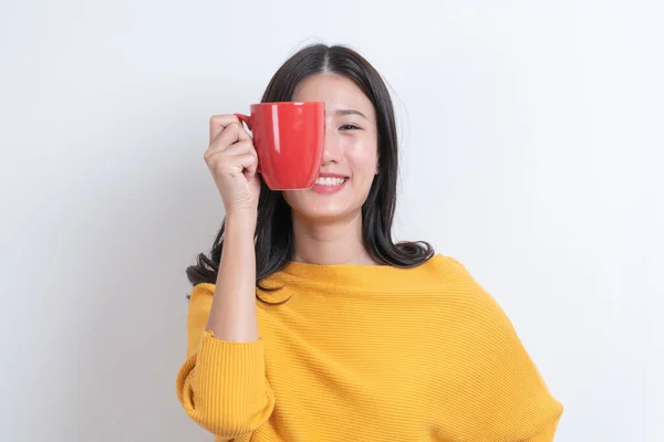 Young asian woman in yellow sweater holding a red cup of coffee, smell good and enjoy the coffee with white background