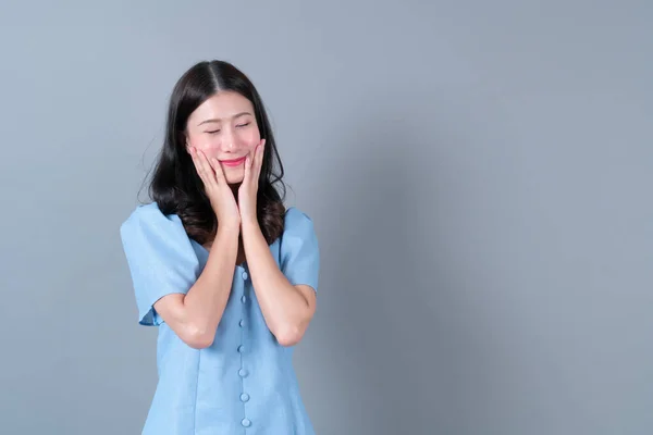 Young asian woman with thinking and happy face in blue dress on grey background