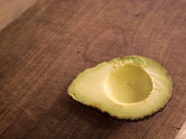 Aguacate cortado por la mitad descansando sobre una tabla de cortar de madera, listo para ser comido — Foto de Stock