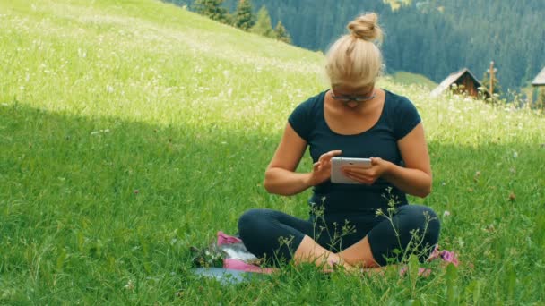 Chica rubia charlando con la tableta en un césped verde — Vídeos de Stock