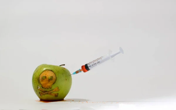 Spuit ingevoegd in een groene appel met een gegraveerde schedel, representatief beeld van het gebruik van GGO-stoffen in voeding, groenten en fruit — Stockfoto