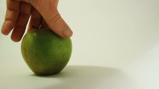 En hand vänder ett grönt äpple med en graverad skalle, en representativ bild av användningen av gmo ämnen i livsmedel, grönsaker och frukt — Stockvideo