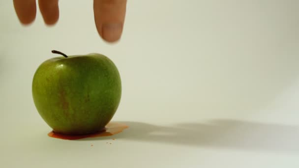 Una mano gira una manzana verde con un cráneo ensangrentado inciso, una imagen representativa del uso de sustancias gmo en alimentos, verduras y frutas — Vídeos de Stock