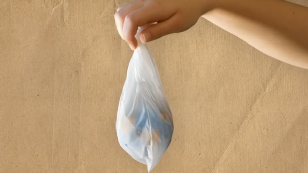 Una adolescente sostiene una bolsa de plástico en su mano que contiene un mini globo, papel reciclado de fondo, material de archivo adecuado para contar sobre problemas de ecología y respeto por la naturaleza y el mundo — Vídeos de Stock