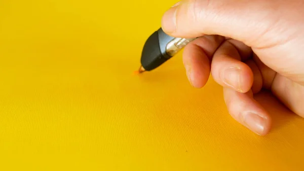 Una mano mans dibuja con una pluma impresora 3d sobre un fondo amarillo, material de archivo ideal para temas como la innovación, la tecnología Imagen De Stock