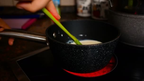 Jovem pastelaria aquece leite em uma panela, filmagem ideal para representar pastelaria caseira — Vídeo de Stock