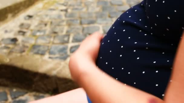 Zwangere vrouw zittend, gekleed in een polka dot moederschap jurk strelen haar buik met haar hand — Stockvideo