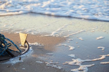 Gün batımında kumlu bir okyanus sahilinde eski bir tekne çapası.