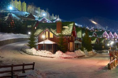 Karda ahşap kulübe ve kış akşamları çelenklerle. Tatil için bir ev ve ormanda tatiller..