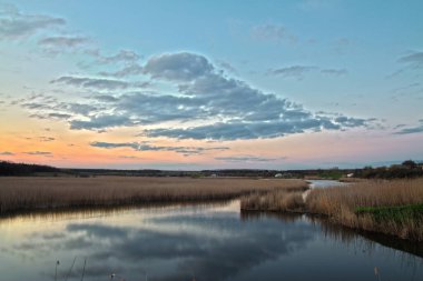 Uzun bir nehrin üzerinde doğa akşam batımı. Sazlık ve baston. Suya yansıyan güzel bulutlar.