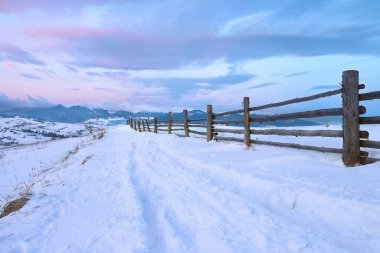 Dağlardaki güzel kış manzarası. Gün doğumu. Karla kaplı yollar ve ahşap çitler.