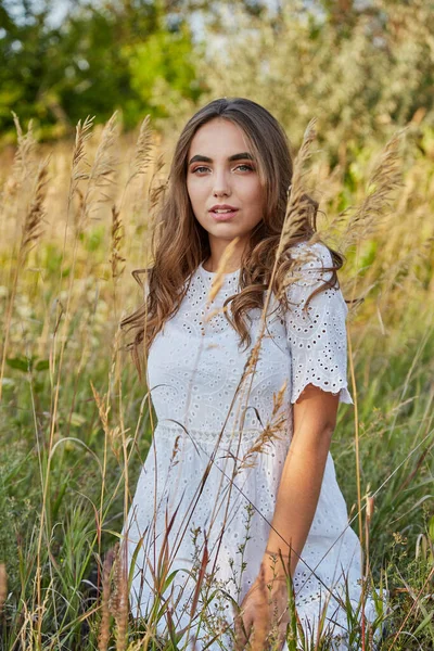 Uzun beyaz elbiseli kız gün batımında gün batımında yol kenarında duran yaz güneşine seviniyor..