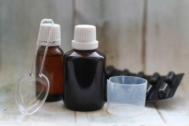 Kahverengi ilaç şişesi ile ölçü kabı ve kaşık