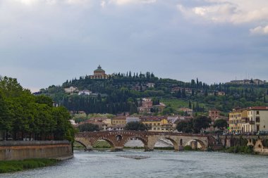 Adige Nehri üzerinde kemerli bir köprü ile Verona Skyline. Nehirde bir viraj ve bir köprü ile parlak şehir manzarası.