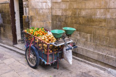A cart by a Moroccan street fruit vendor equipped with scales for weighing fruits, filled with tangerines and grenades on a narrow medina street in the city of Fez, Morocco clipart
