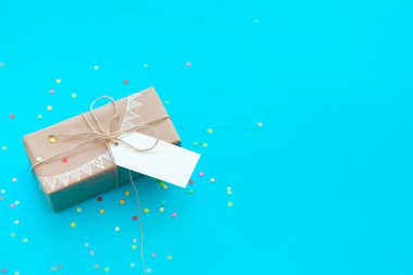 Zanaat broun hediye kutusu. Renkli bir çelenk, bayrakları çizim. Arka plan mavi ve turkuaz. Konfeti.