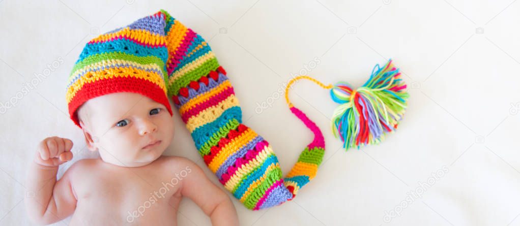 A baby one month is lying on a white background. Rainbow cap of the gnome.