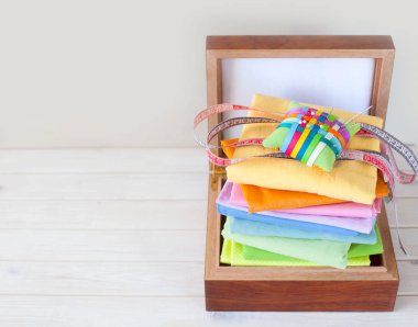 Renkli kumaş katlanmış yığını. İğne yatak, makas, ölçüm bandı. Bej renkli arka plan.