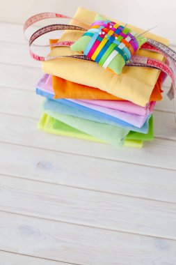 Renkli kumaş katlanmış yığını. İğne yatak, makas, ölçüm bandı. Bej renkli arka plan.