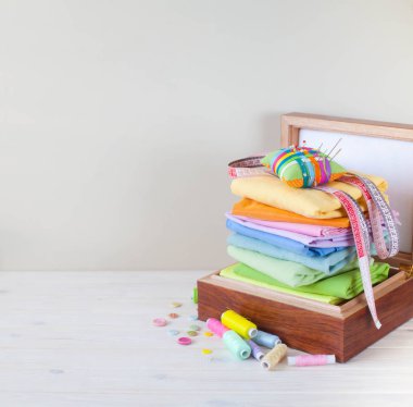 Renkli kumaş katlanmış yığını. İğne yatak, makas, ölçüm bandı. Bej renkli arka plan.