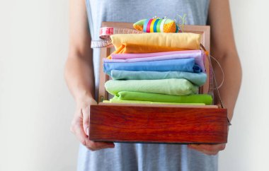 Renkli kumaşlarla yığını tutan bir kadın. İğne yatağı, makas, bant ölçme. Bej arka plan.