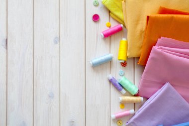 Renkli kumaş katlanmış yığını. İğne yatak, makas, ölçüm bandı. Bej renkli arka plan.