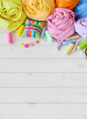 Renkli kumaş katlanmış yığını. İğne yatak, makas, ölçüm bandı. Bej renkli arka plan.