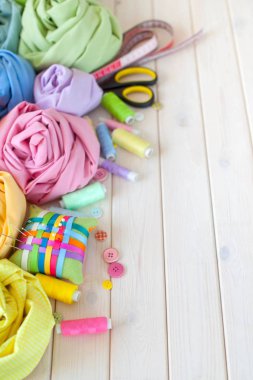 Renkli kumaş katlanmış yığını. İğne yatak, makas, ölçüm bandı. Bej renkli arka plan.