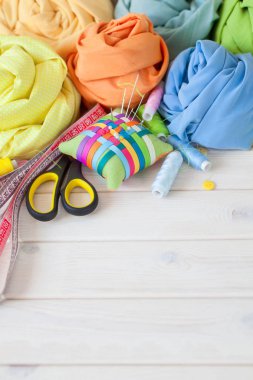 Renkli kumaş gül çiçek şeklinde katlanmış. Makas, bant ölçü, iğne, iğne mili, düğmeleri.