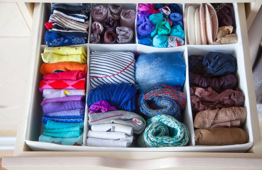 Neatly folded clothes with accessories in chest of drawers
