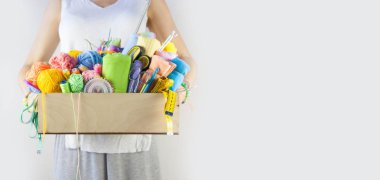 Kadın sepet dolusu aksesuarı ahşap masa üzerinde dikiş işi için tutuyor.