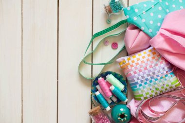 Dikiş aksesuarları beyaz bir arka plan üzerinde yalan. Ölçüm bandı, iplik, kumaş ve Dikiş iğneler. Kumaş pembe, nane ve turkuaz.
