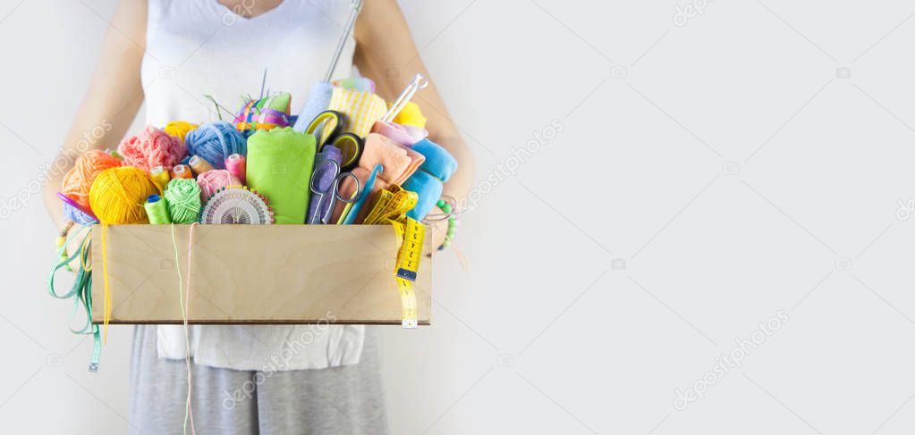 woman holds basket with accessories for needlework on wooden table