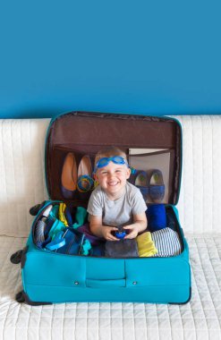 Turkuaz bir bavulun içinde oturan çocuk.