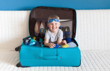 Turkuaz bir bavulun içinde oturan çocuk.