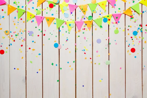 Colored flags garlands with confetti against white wooden background